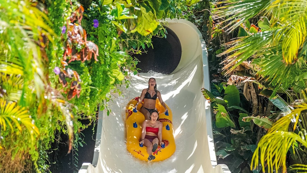 Visitors enjoying a water slide at Siam Park, surrounded by lush greenery.