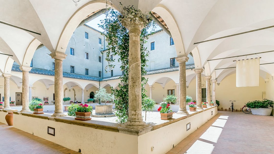 Courtyard of Palazzo Piccolomini with arches and potted plants, part of all-inclusive pass.