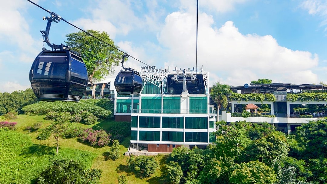 Singapore Cable Car passing Mount Faber Peak station amidst lush greenery.