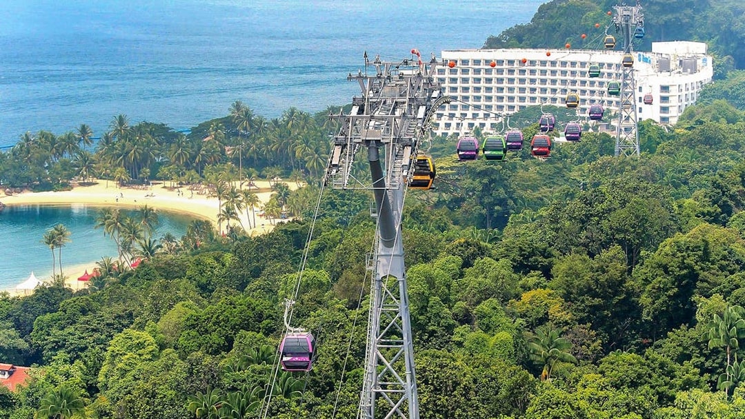 Singapore Cable Car over lush greenery and beach, with ocean view in the background.