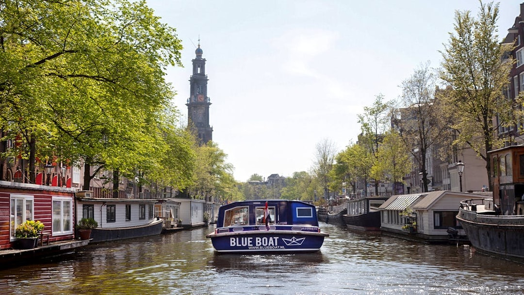 Blue boat cruising Amsterdam canal with Westerkerk tower in view.