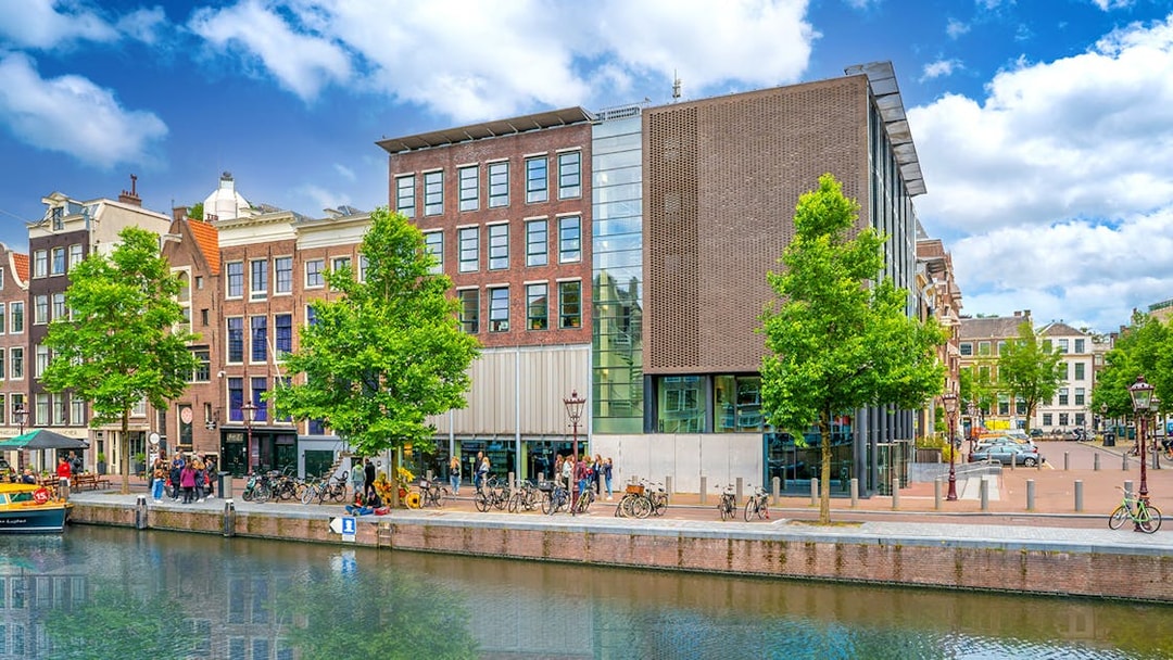 Anne Frank House exterior along Amsterdam canal with visitors and bicycles.
