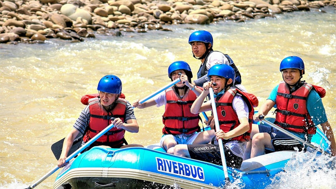 White water rafting group on Kampar River, Malaysia, navigating rapids in a blue raft.