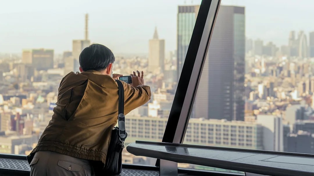 Tourist photographing Tokyo skyline from Tokyo Tower observation deck.