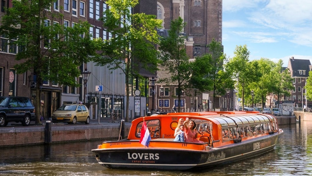 Sightseeing boat on Amsterdam canal with passengers waving, historic buildings in background.