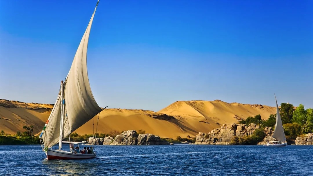 Felucca sailing on the Nile River with desert landscape in the background, Egypt.