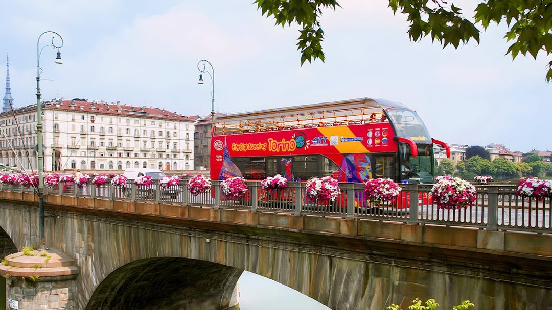 Turin hop-on hop-off bus crossing a bridge with cityscape in the background.