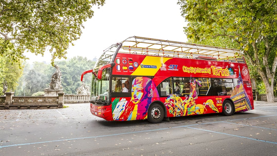 Turin hop-on hop-off bus near a park with statues and trees.