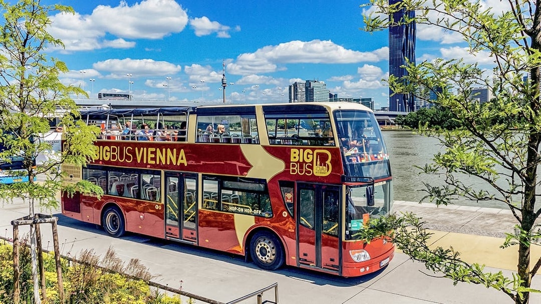Tourists on Big Bus Vienna passing by the Danube River with city skyline in view.