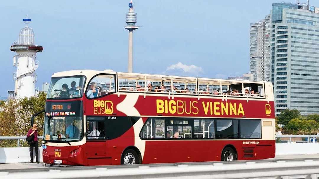 Tourists on Big Bus Vienna with Ferris Wheel and Danube River Cruise in background.