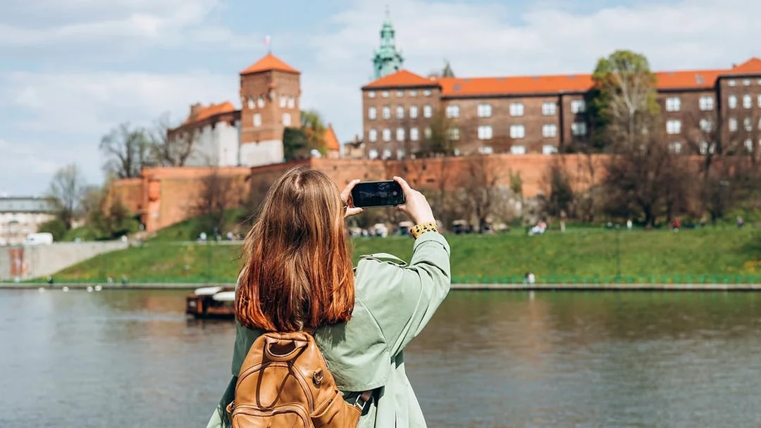 Tourist photographing Wawel Castle from across the Vistula River in Krakow.
