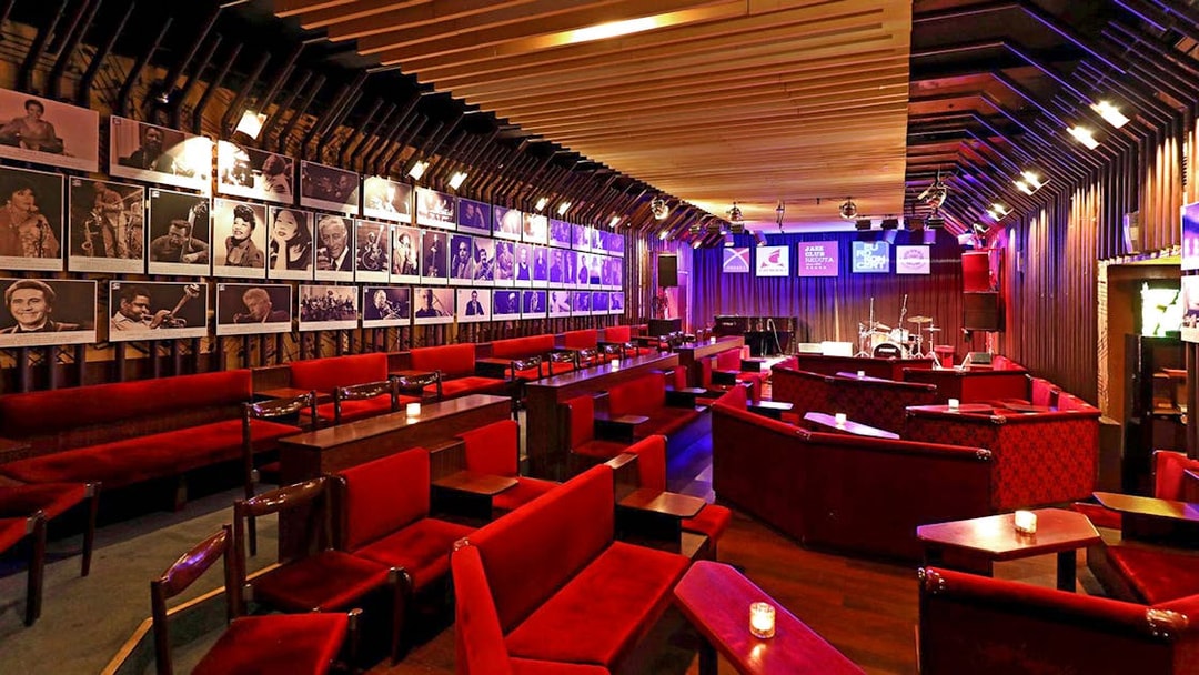 Interior of Reduta Jazz Club with red seating, stage, and musician portraits on walls.