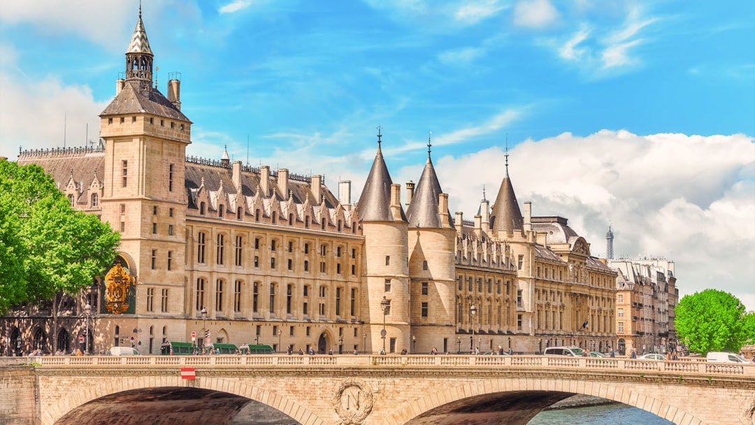 Conciergerie in Paris with historic architecture and Seine River bridge.