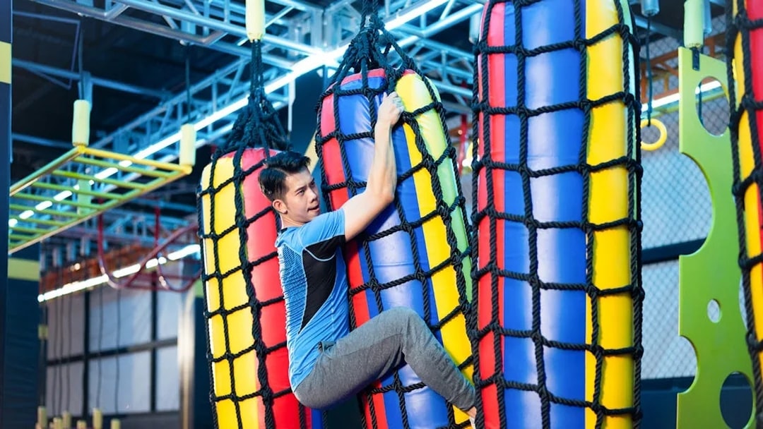 Man climbing colorful rope bag in indoor adventure park.