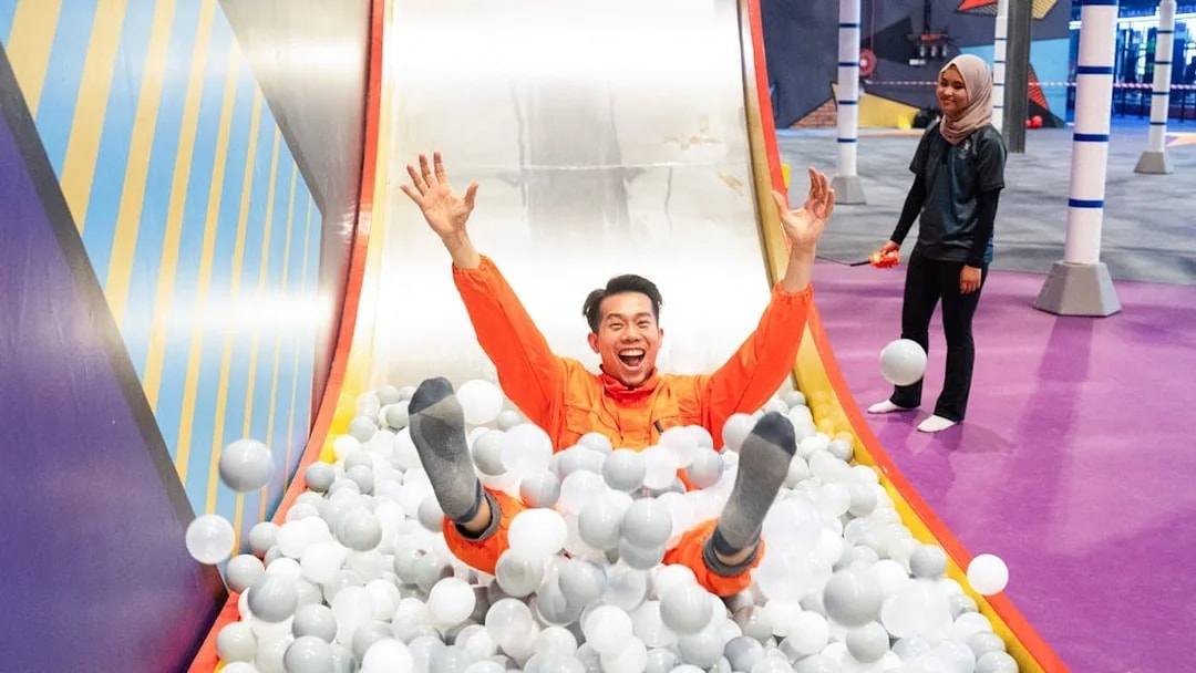 Visitor sliding into ball pit at indoor playground.