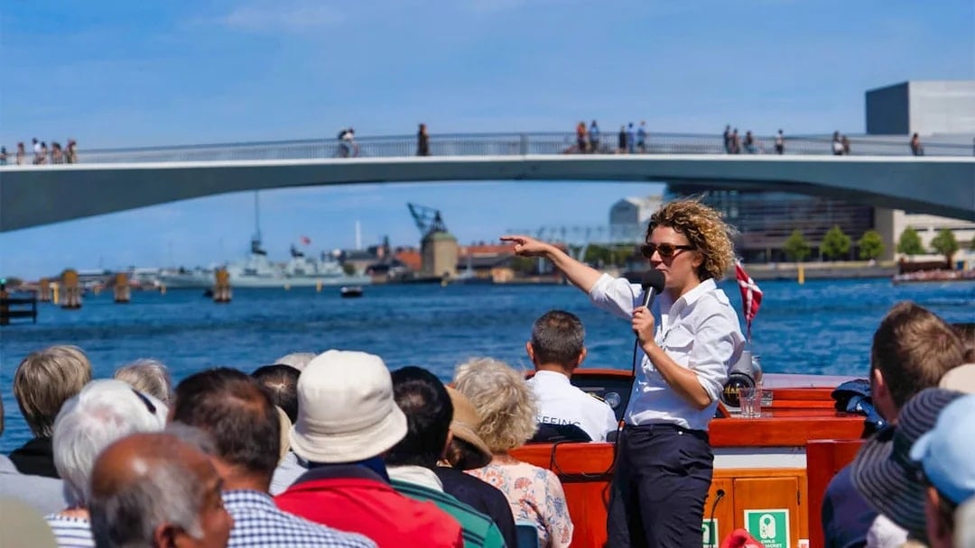 Tour guide speaking to passengers on a boat near a bridge in Copenhagen.