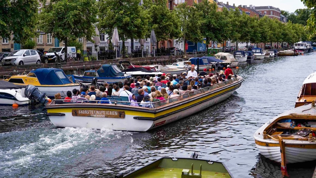 Boat tour on Copenhagen canal with tourists, passing colorful buildings and moored boats.