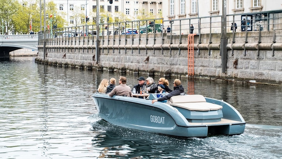 Guests on an electric boat tour in Copenhagen, viewing city canals while captain pedals.