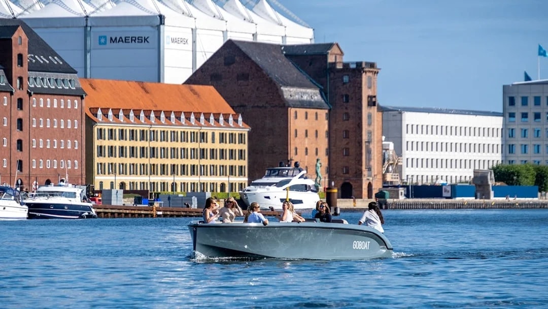 Guests on a boat tour in Copenhagen harbor with historic buildings in the background.