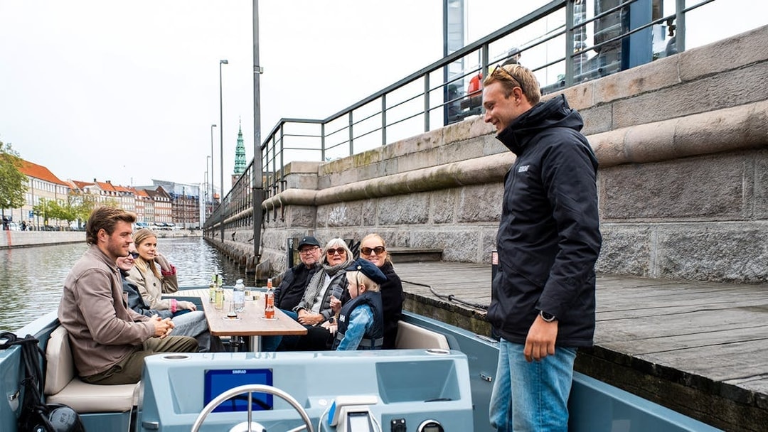 Guests on an electric boat tour in Copenhagen with captain pedaling along the canal.