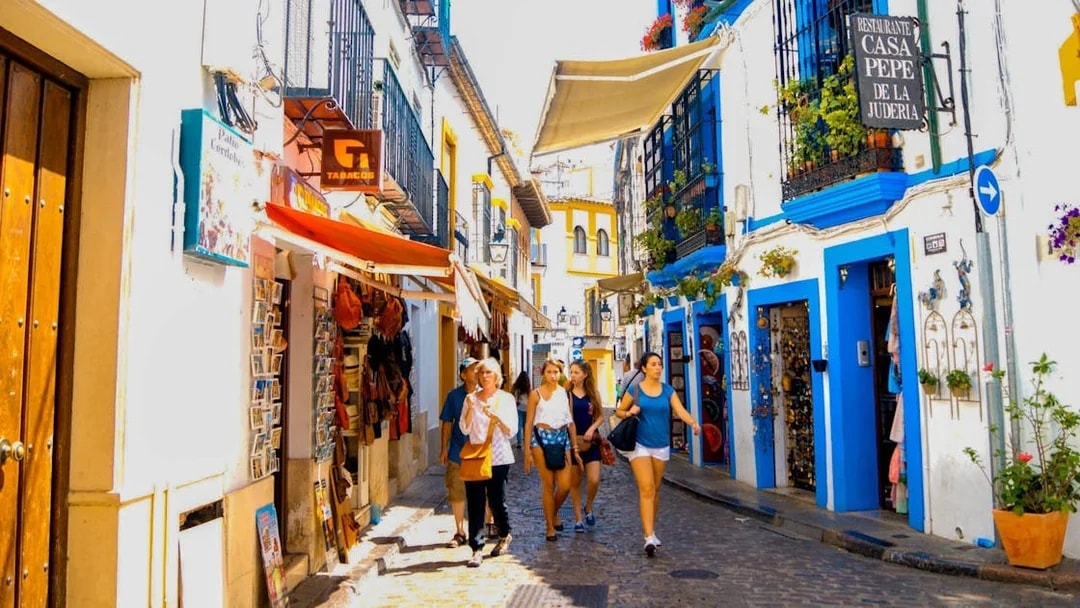 Narrow street in Cordoba with tourists walking, colorful buildings, and local shops.