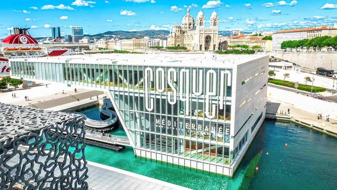 Cosquer Cave building in Marseille with waterfront view and cathedral in background.