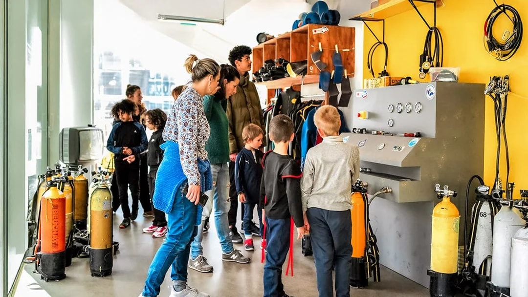 Visitors exploring diving equipment at Cosquer Cave exhibit in Marseille.