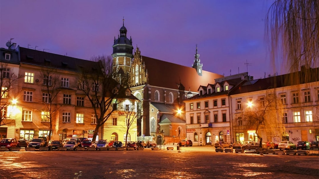 Krakow city square at dusk with illuminated historic buildings and church tower.