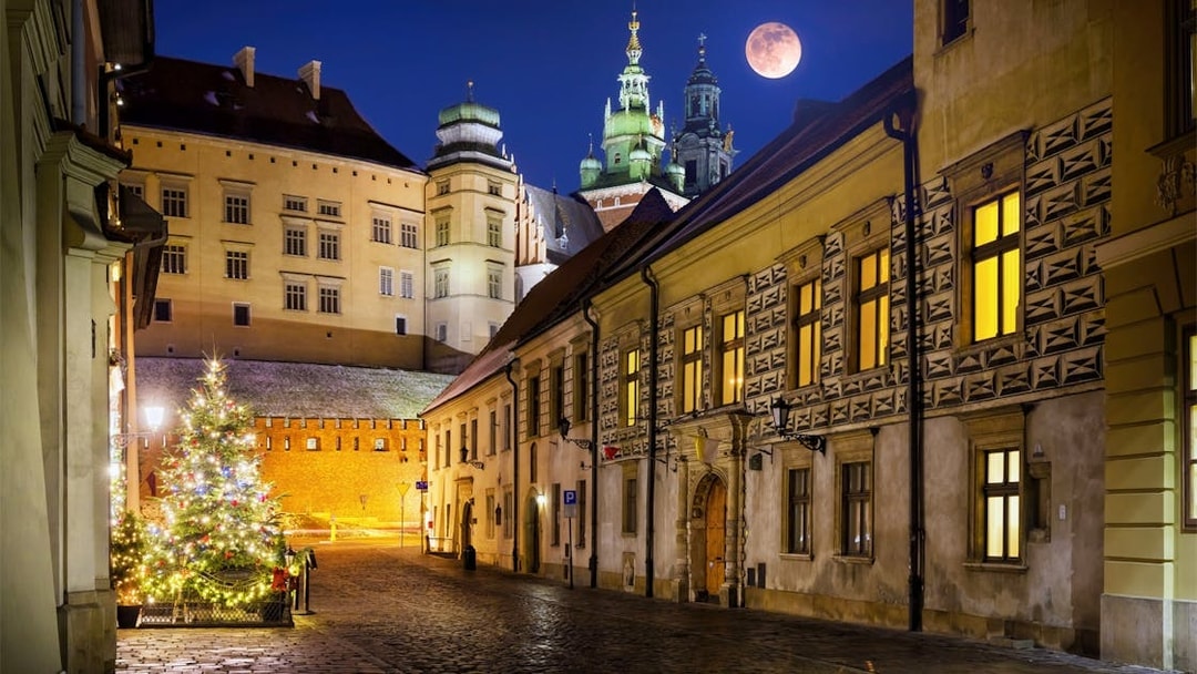 Krakow street at night with illuminated buildings and a full moon.