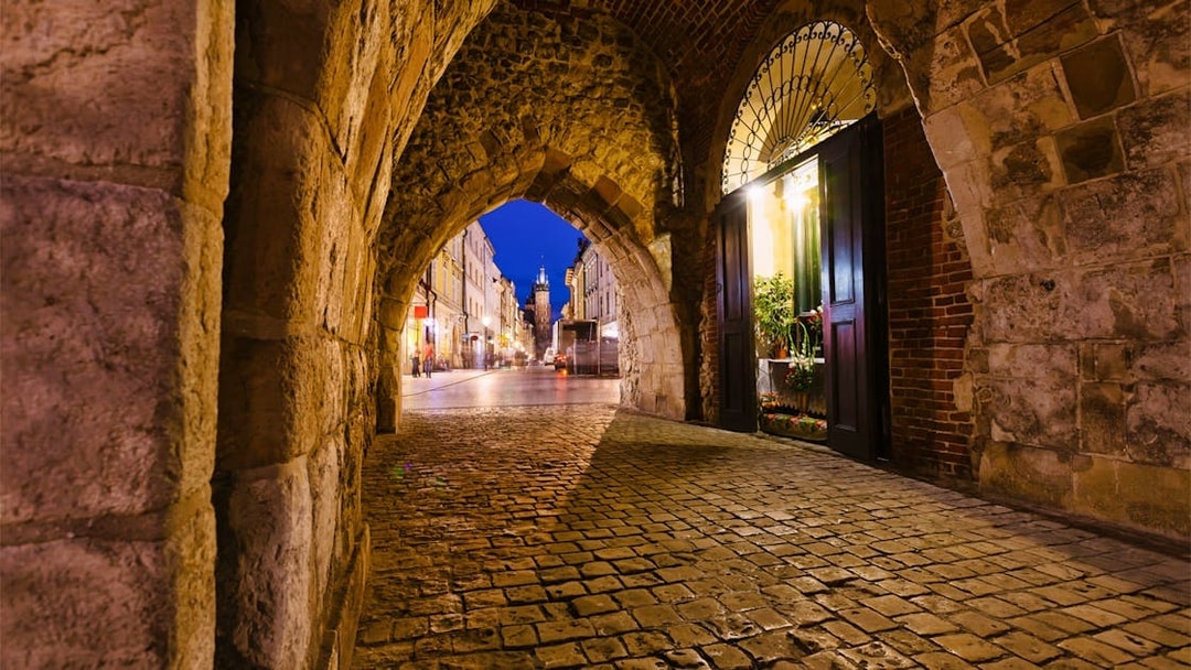 Krakow city street view through a stone archway at night.
