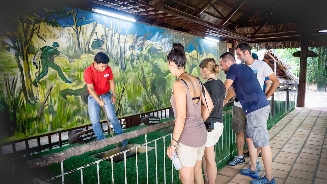 Guide demonstrating booby trap mechanism to tourists at Cu Chi Tunnel, Vietnam.