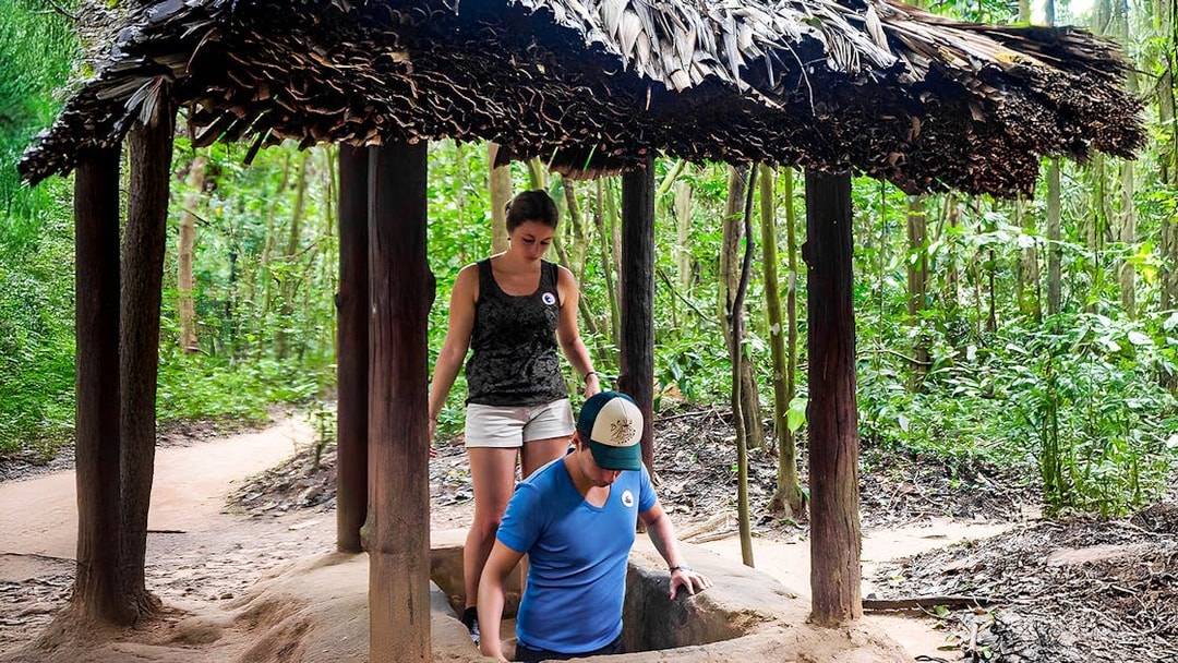 Visitors entering Cu Chi tunnel with guide in Vietnam forest.