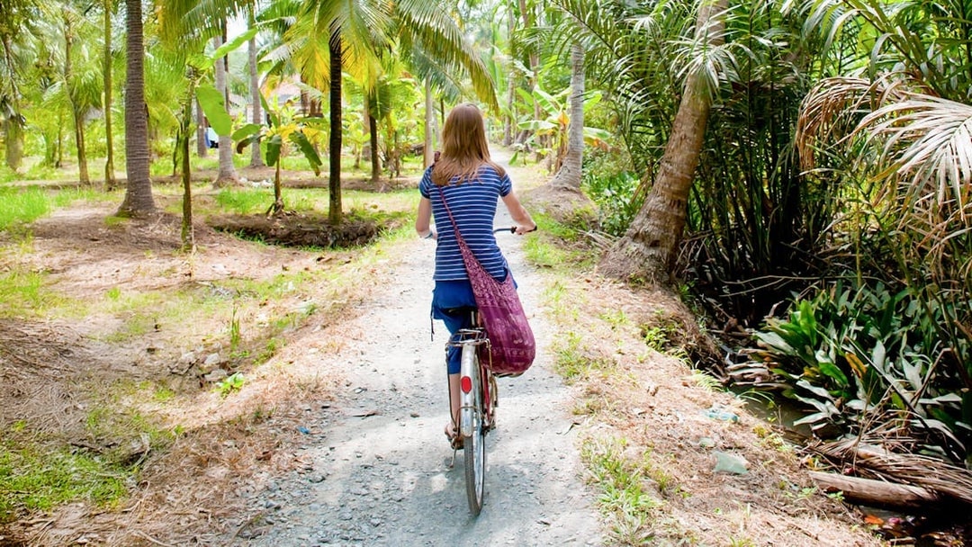 Tourist cycling through palm trees in My Tho, Mekong Delta.