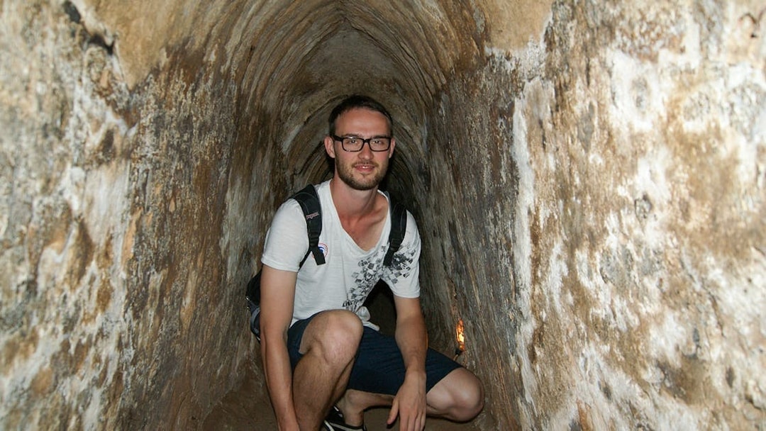 Young tourist crouching inside narrow Cu Chi tunnel in Vietnam.