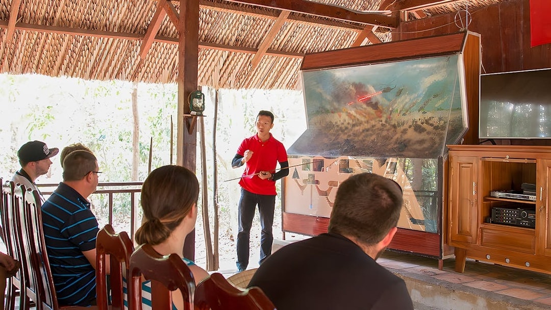 Guide explaining Vietnam war strategies at Cu Chi Tunnels to tourists.