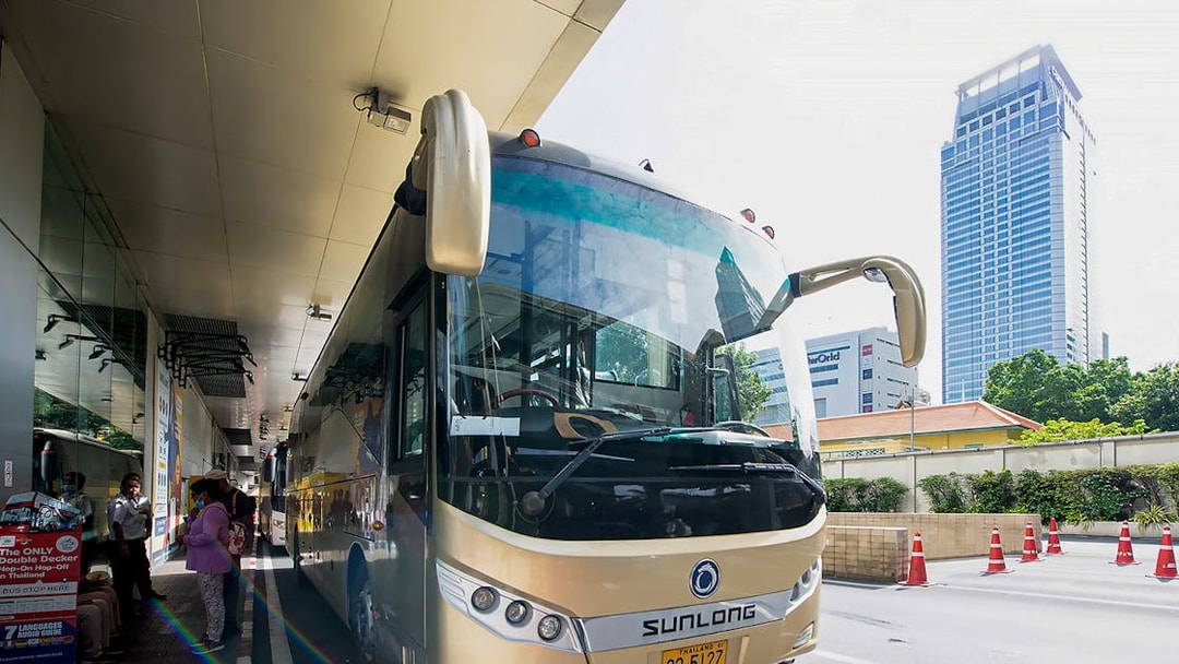 Tour bus parked at a station in Bangkok, Thailand, with passengers boarding.