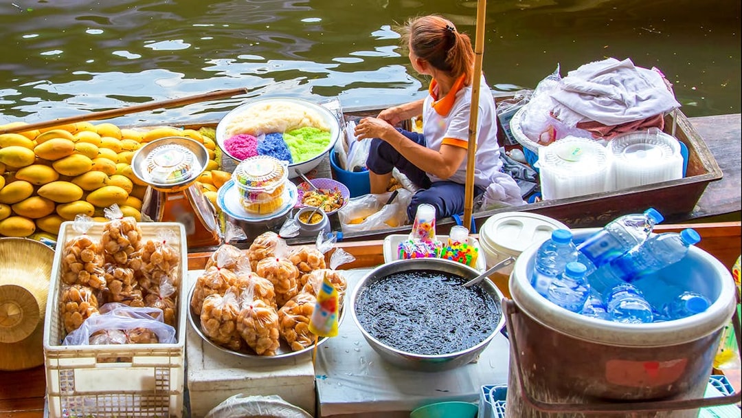 Vendor selling colorful desserts and snacks at Damnoen Saduak Floating Market, Thailand.