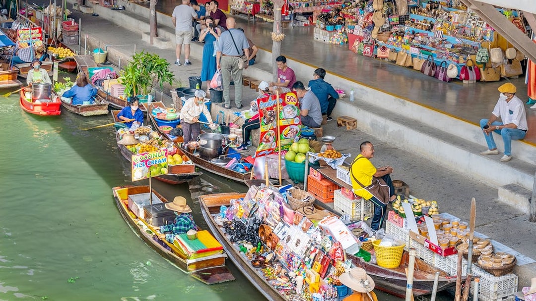 Boats selling goods at Damnoen Saduak Floating Market, Thailand, with vendors and tourists.