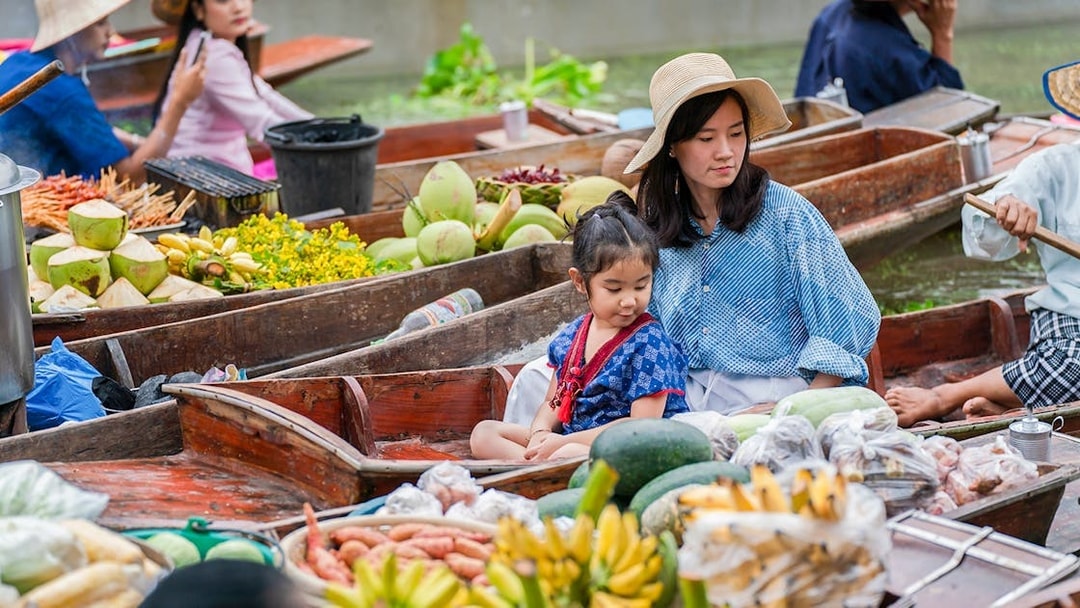 Asian tourists in a boat at a floating market with tropical fruits in Thailand.