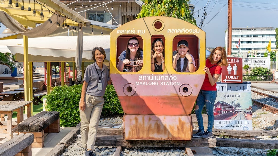 Visitors posing with a train cutout at Maeklong Railway Market station.