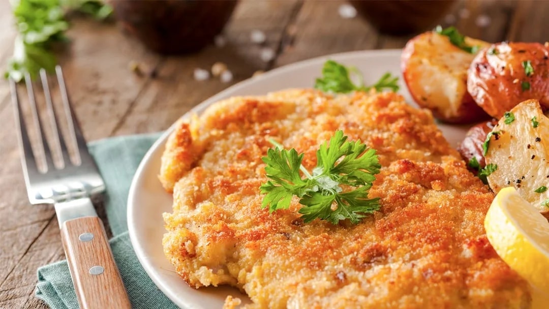 Wiener Schnitzel with roasted potatoes and lemon slice on a plate.