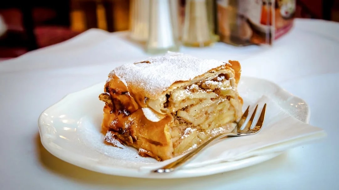 Slice of apple strudel with layers of apples and spices on a plate.