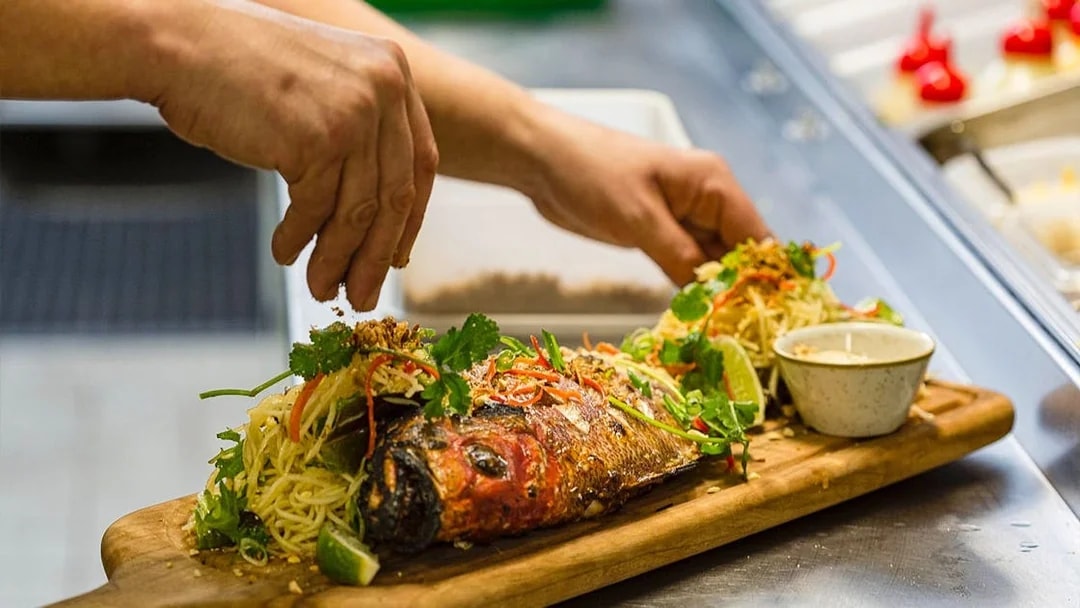 Gourmet fish dish being prepared on a wooden board during a culinary tour.