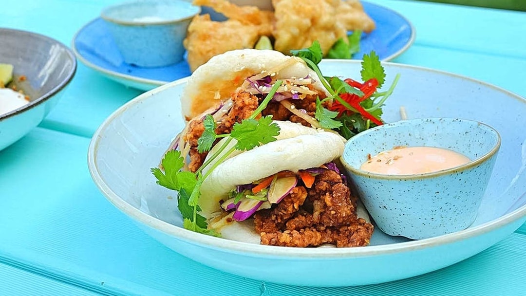 Gourmet bao buns with crispy filling and dipping sauce on a blue plate.