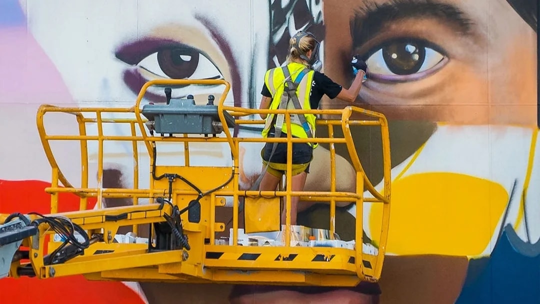 Artist painting a large mural on a lift during a 3.5-hour gourmet lunch or dinner and art tour.