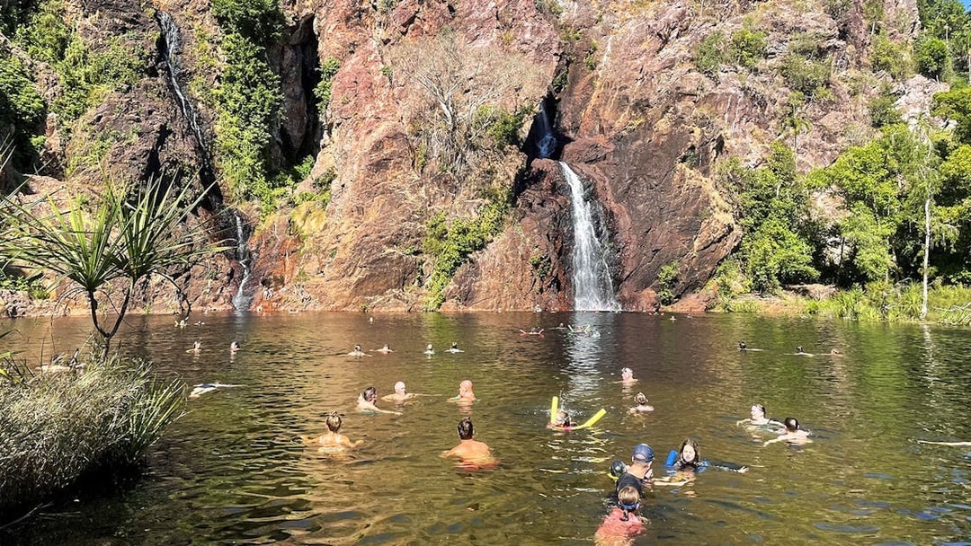 Visitors swimming near a waterfall in Litchfield National Park, Australia.