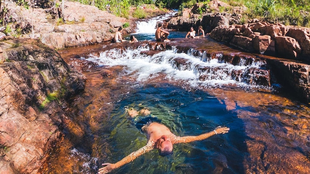 Visitors swimming in a natural pool at Litchfield National Park, surrounded by rocky terrain.