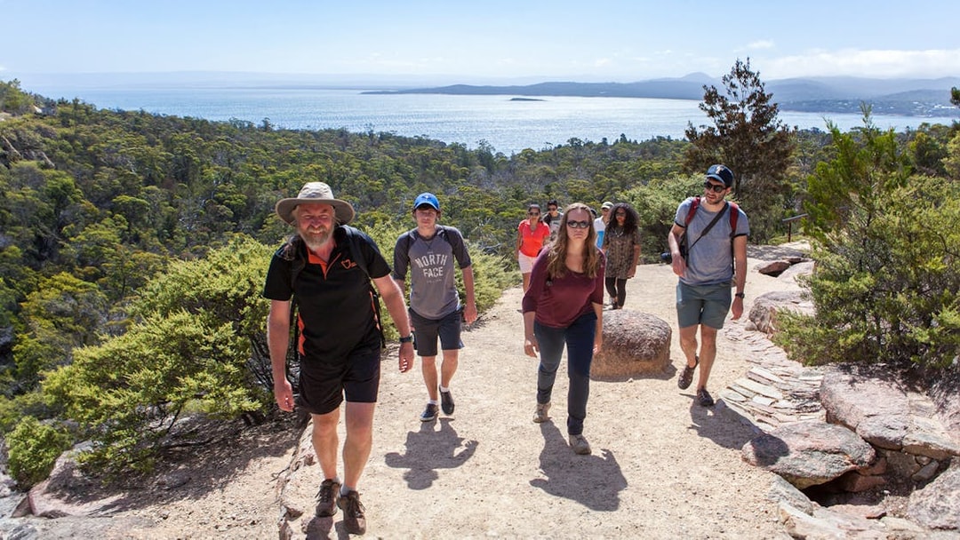 Group hiking on a trail with views of Wineglass Bay, Tasmania.