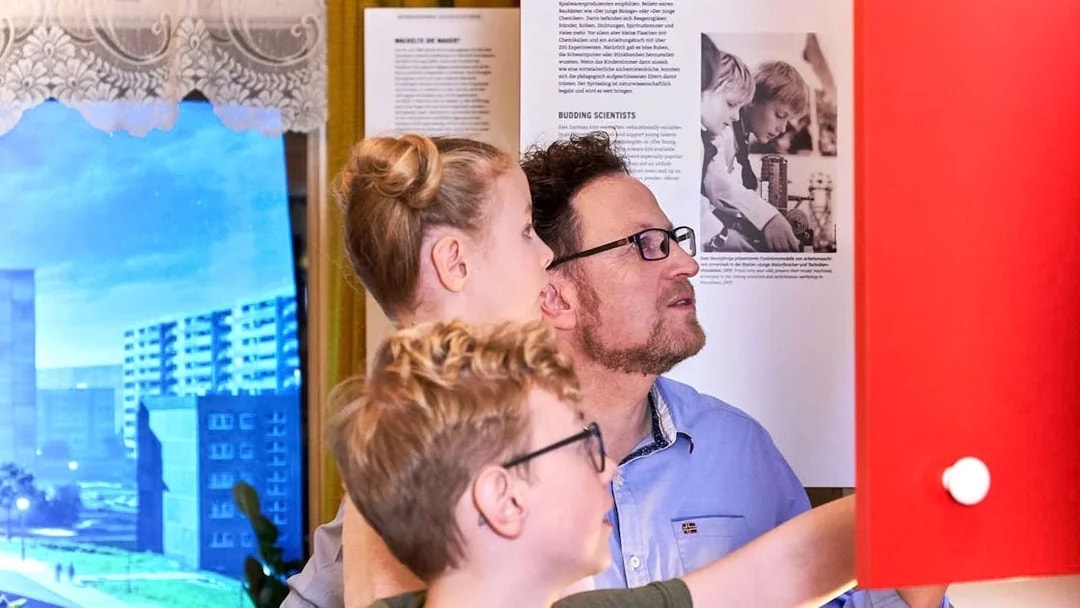 Father and kids exploring interactive exhibit at DDR Museum, Berlin.