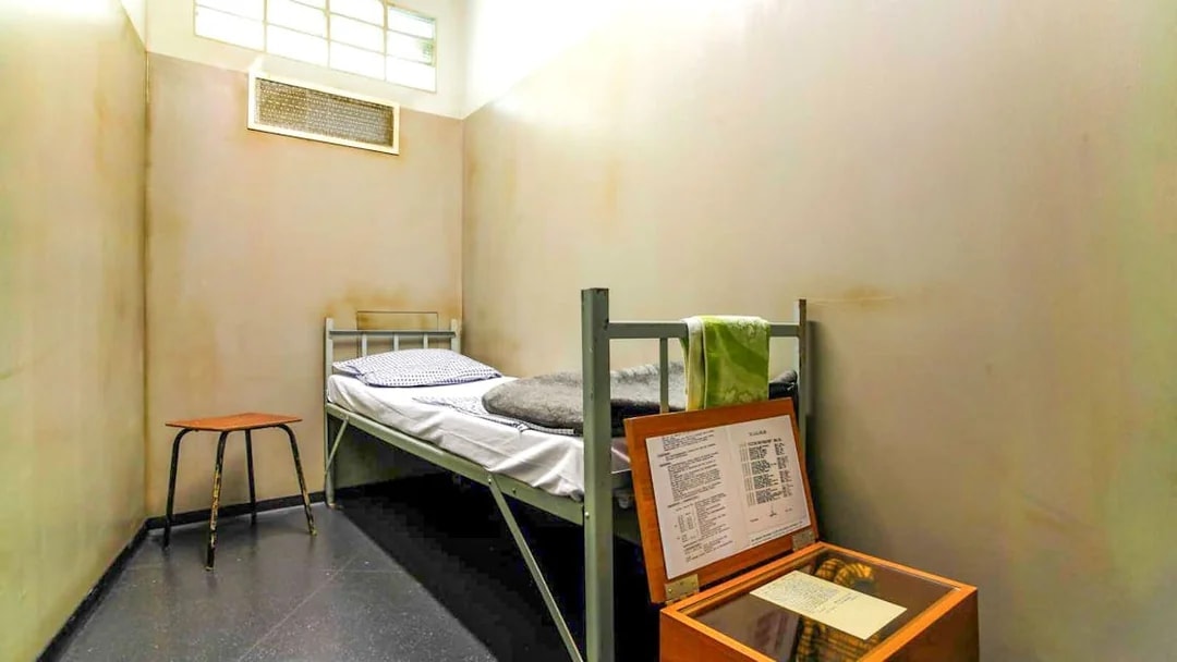 DDR Museum Berlin exhibit showing a recreated prison cell with a bed and documents.